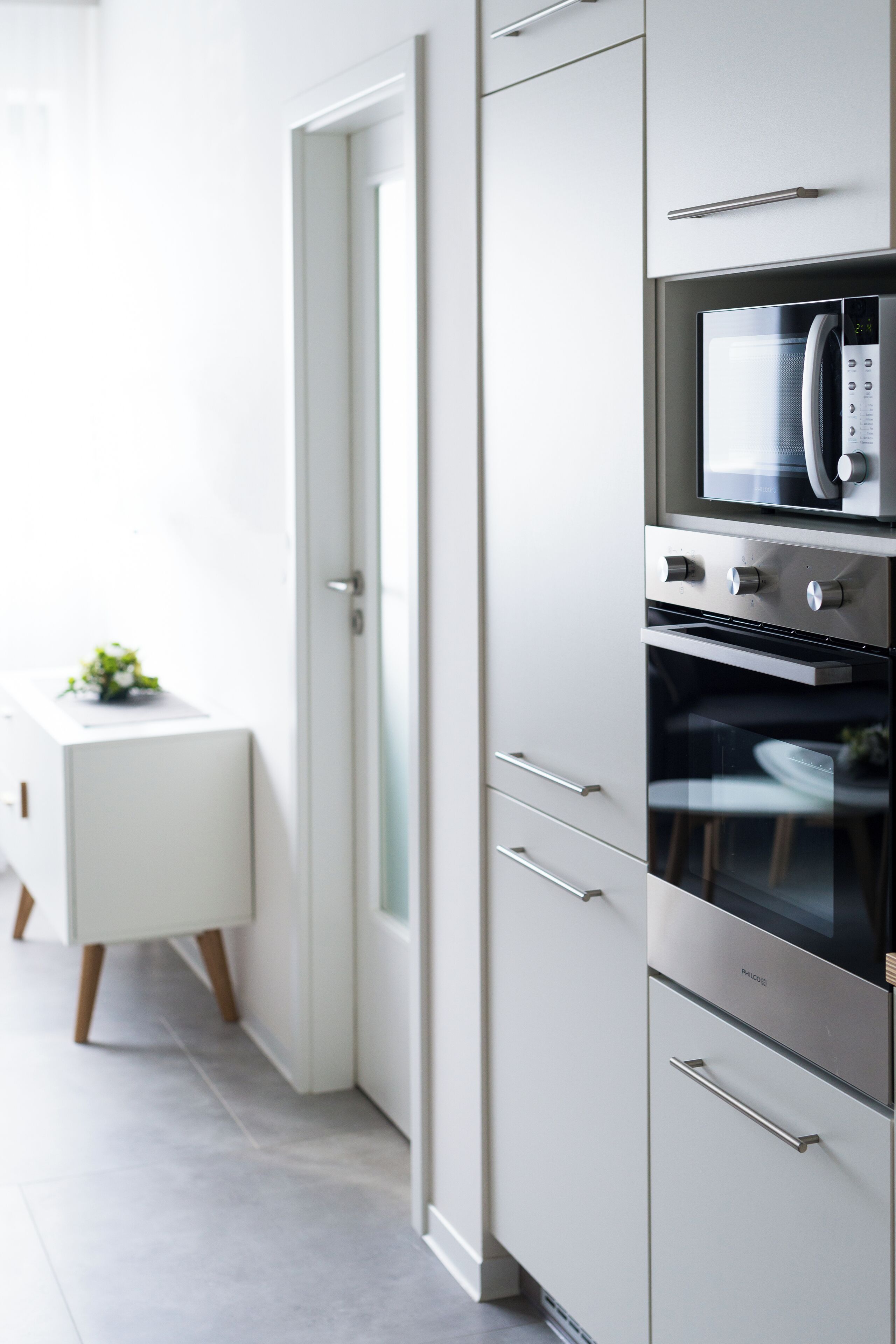 Una cocina moderna con electrodomésticos de acero inoxidable, encimera blanca y una puerta que da a otra habitación.
