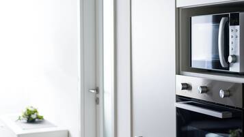 Una cocina moderna con electrodomésticos de acero inoxidable, encimera blanca y una puerta que da a otra habitación.