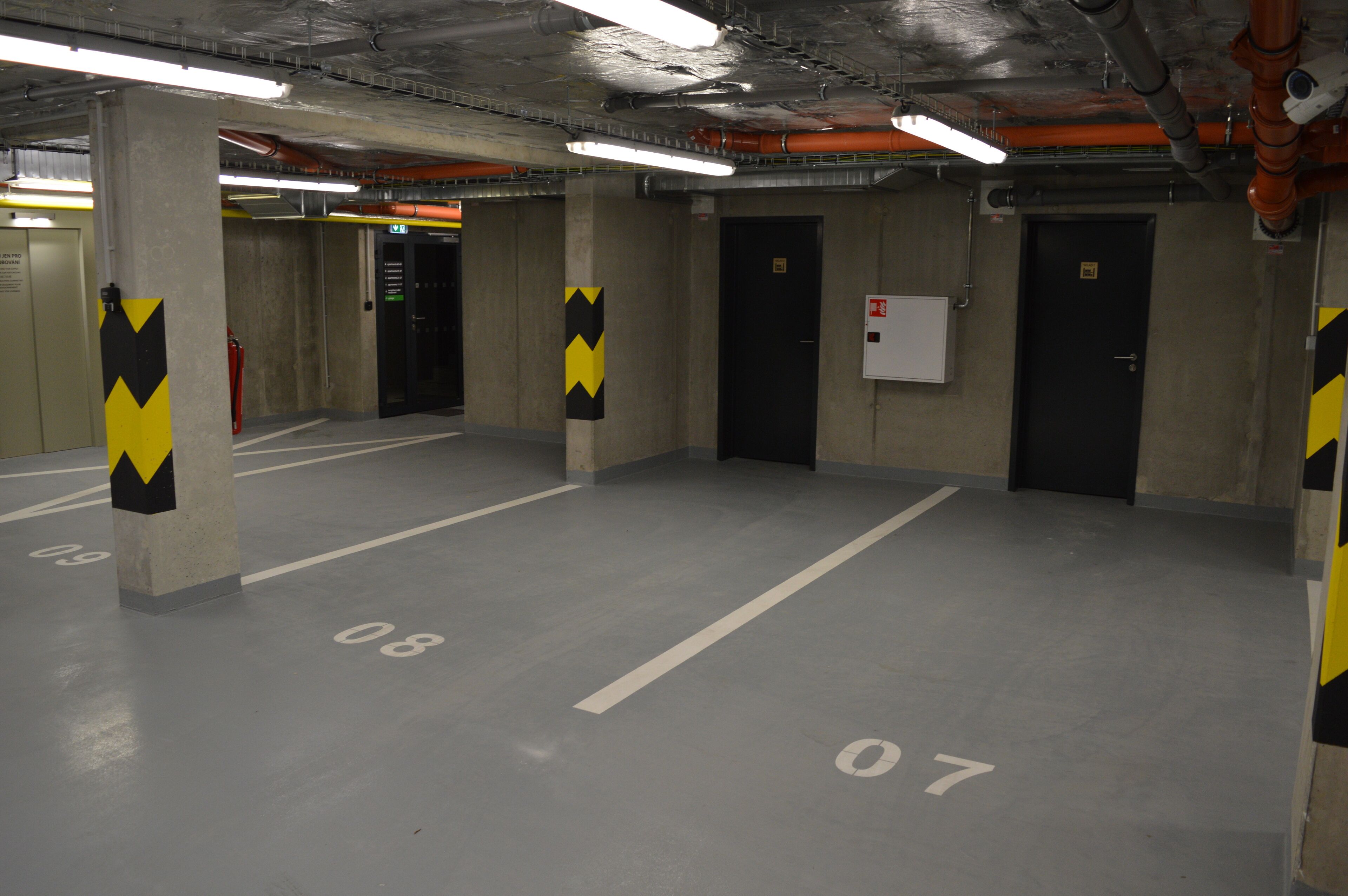 A parking garage with concrete pillars, numbered parking spaces, and emergency equipment.