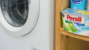 Una lavatrice a carica frontale con pannello di controllo, un contenitore di detersivo Persil e una bottiglia di detersivo Silan.