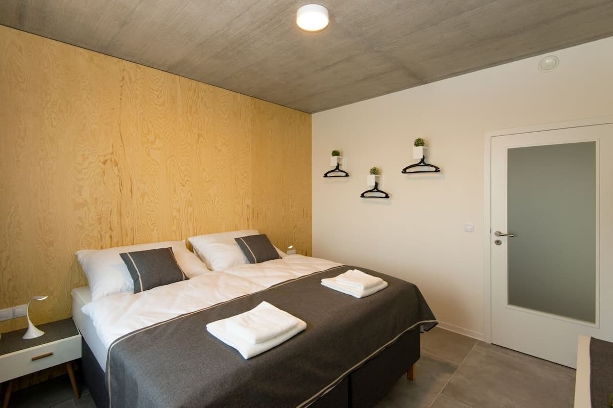 A bedroom with a bed, bedside tables, a nightstand, a door, and wall-mounted plant holders.