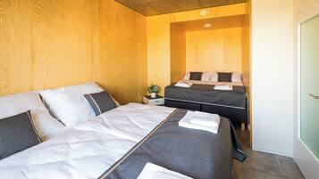A modern hotel room with two beds, wooden paneling on the walls, and a small bedside table with a plant.