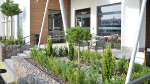 Un edificio moderno con un caffè e un'area reception. Sono presenti posti a sedere all'aperto e un piccolo giardino con diverse piante.