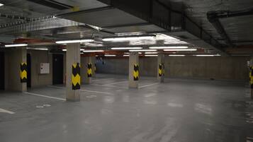 An indoor parking garage with concrete pillars, fluorescent lighting, and marked parking spaces.