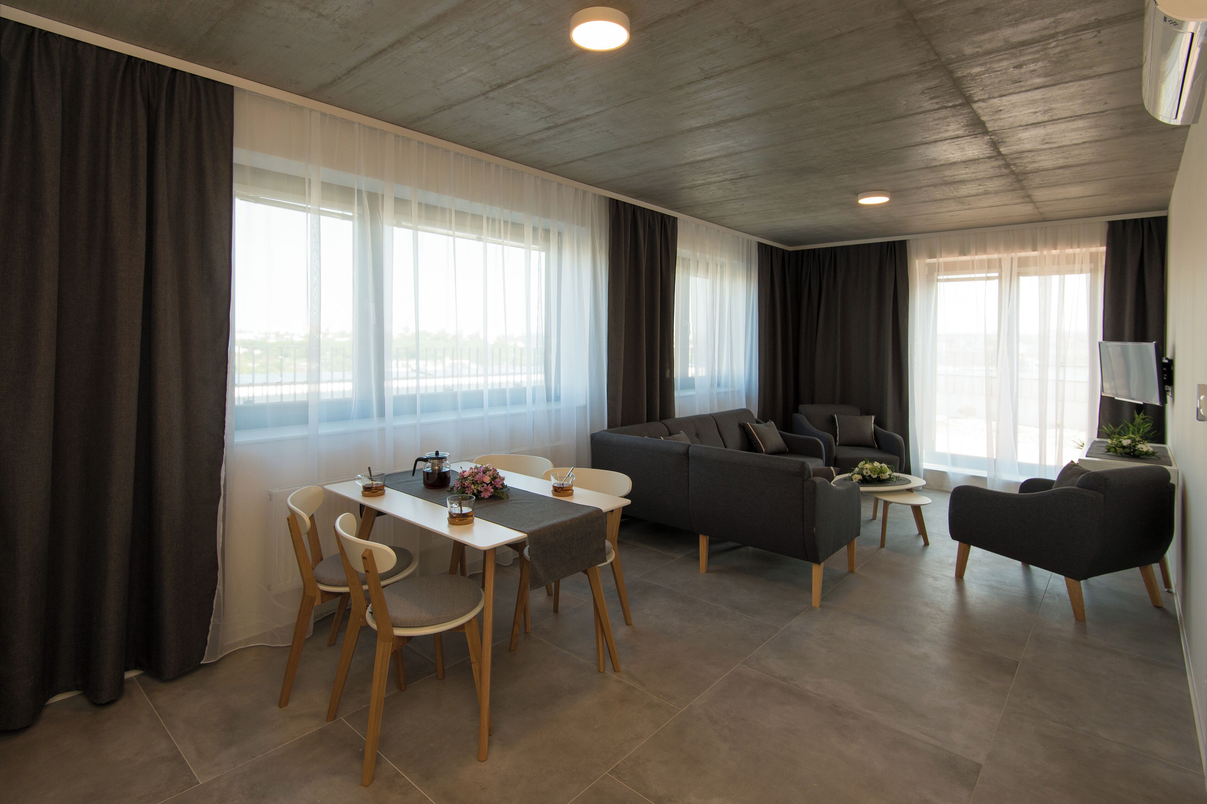 A modern living room with a dining area, grey sofas, wooden chairs, and a coffee table.