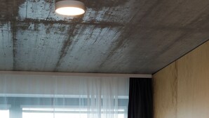 Camera d'albergo con un letto, una finestra con tende leggere e un soffitto con travi a vista.