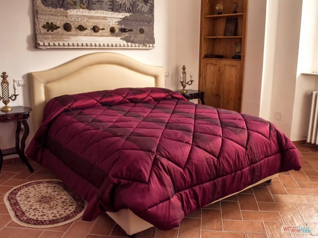 A room with a bed, a wooden cabinet, a rug, and a painting on the wall.