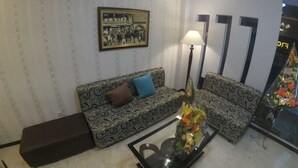 Un salon avec des canapés à motifs, une table basse en verre, une lampe et un tableau encadré au mur.