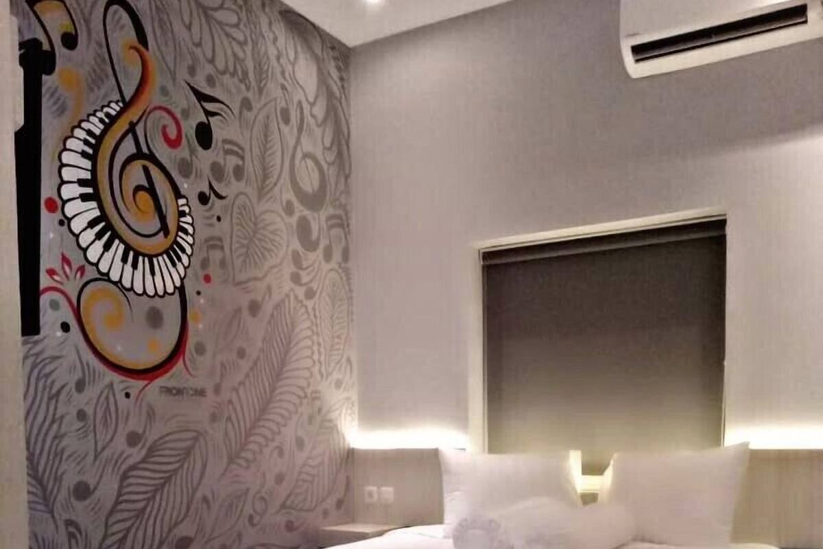 Une chambre d’hôtel moderne avec un grand lit, une tête de lit dotée d’un éclairage intégré et une fresque murale décorative.