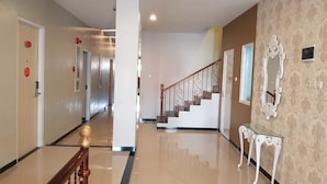 Un couloir d’hôtel avec un sol ciré, une main courante en bois, un escalier et un miroir décoratif accroché au mur.