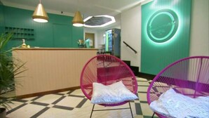Una zona de recepción con mostrador, dos sillas rosas y un letrero de neón en la pared.