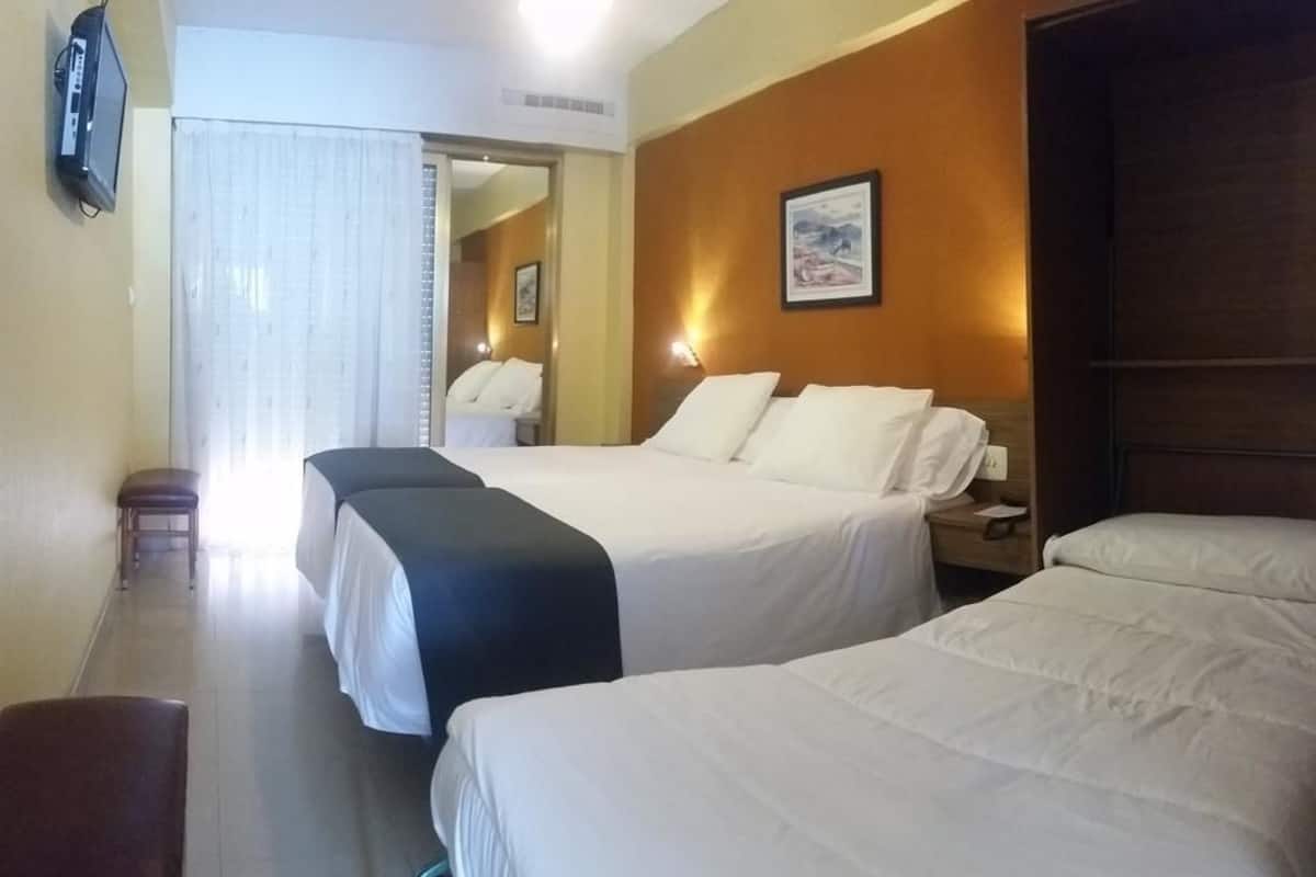 A hotel room with two beds, a television, a mirror, and a painting on the wall.
