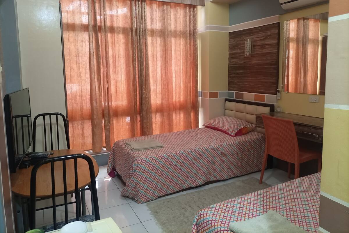A bedroom with two beds, a desk, a chair, and an air conditioning unit.