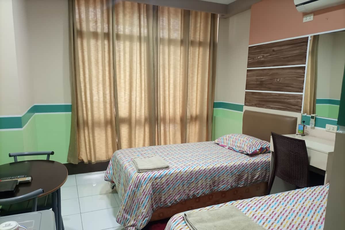 A hotel room with two beds, a desk, a chair, a table, and a window with curtains.