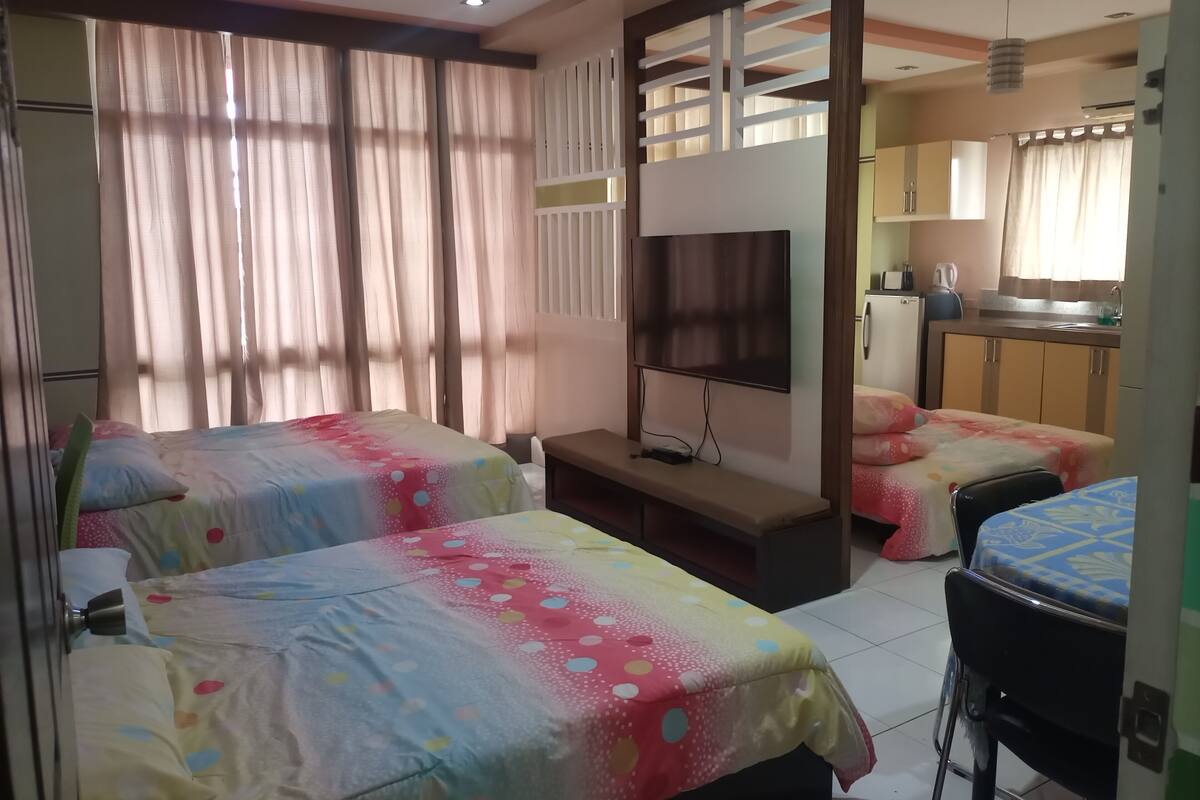 A hotel room with two beds, a TV, a desk, and a kitchenette.