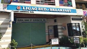 Un immeuble à plusieurs étages doté d’une façade colorée, d’une enseigne indiquant « LIGAO BED & BREAKFAST » et d’une devanture fermée pour la « RURAL BANK OF GUINOBATAN, INC. ».