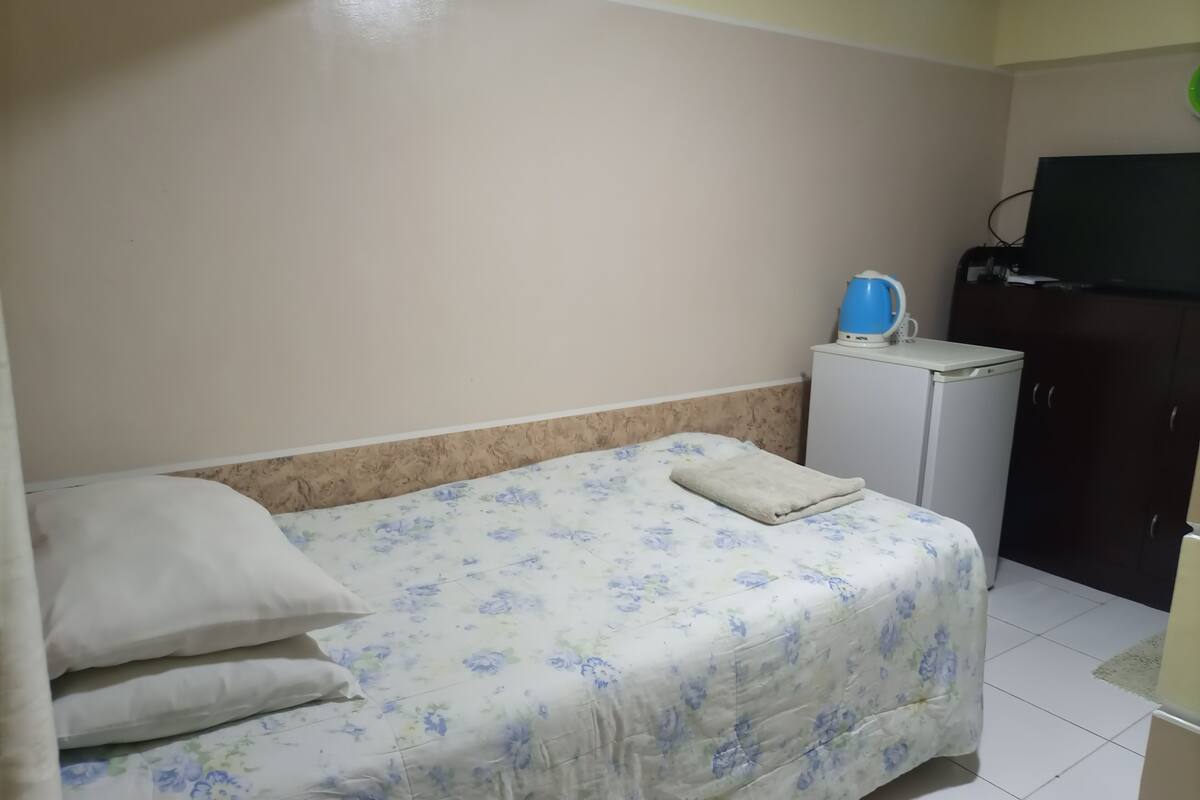 A small, neatly arranged bedroom with a bed, a white cabinet, and a television on a stand.