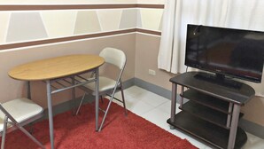 Une petite pièce avec une table en bois, deux chaises, un téléviseur posé sur un meuble et un tapis rouge.