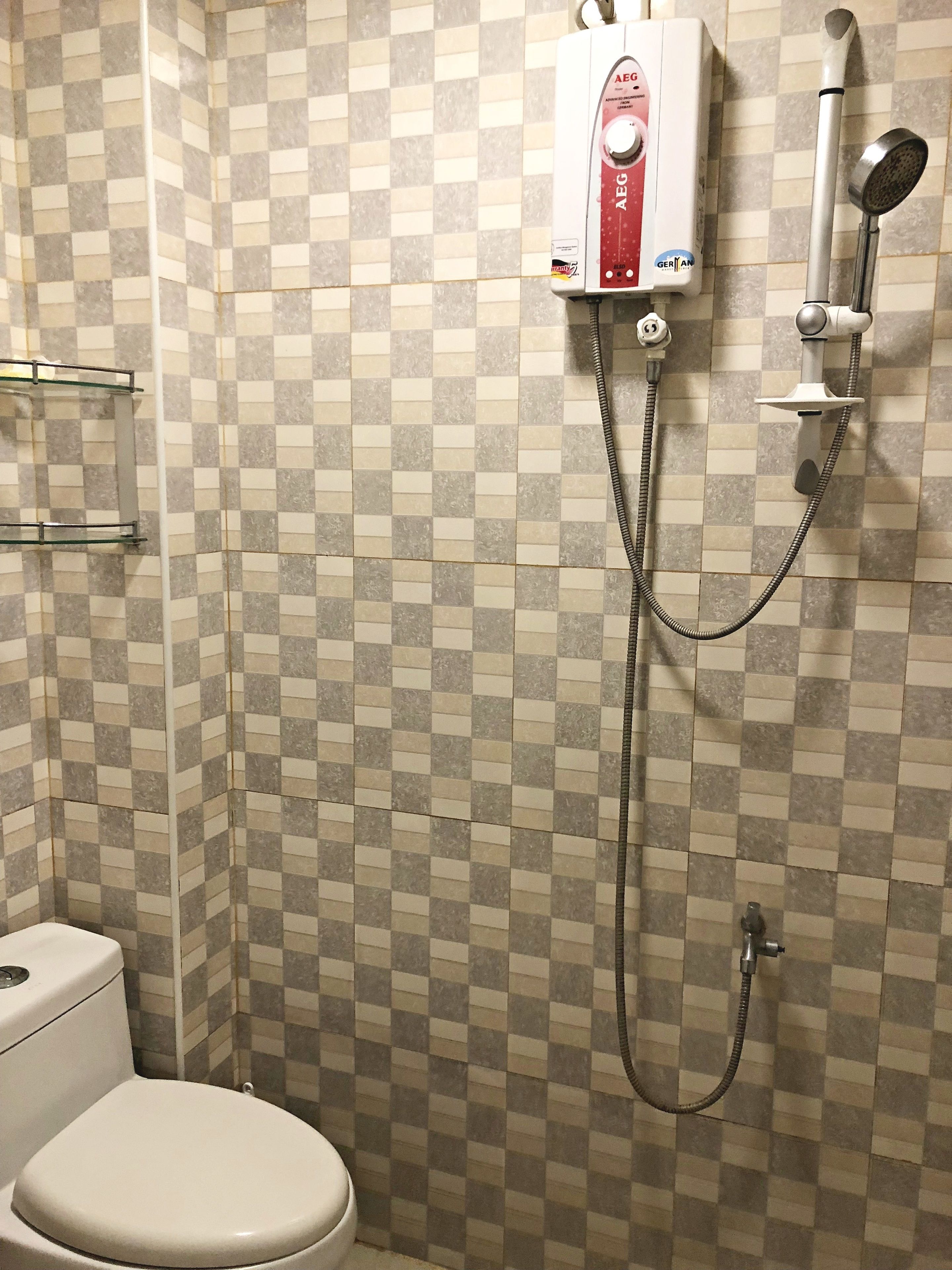 Une salle de bain avec un mur recouvert de carreaux à motifs, des toilettes et une douche équipée d’un flexible.