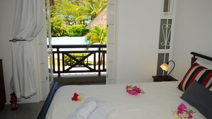 Un dormitorio con cama, mesita de noche con lámpara, ventana con vista a una piscina y palmeras, y un extintor.