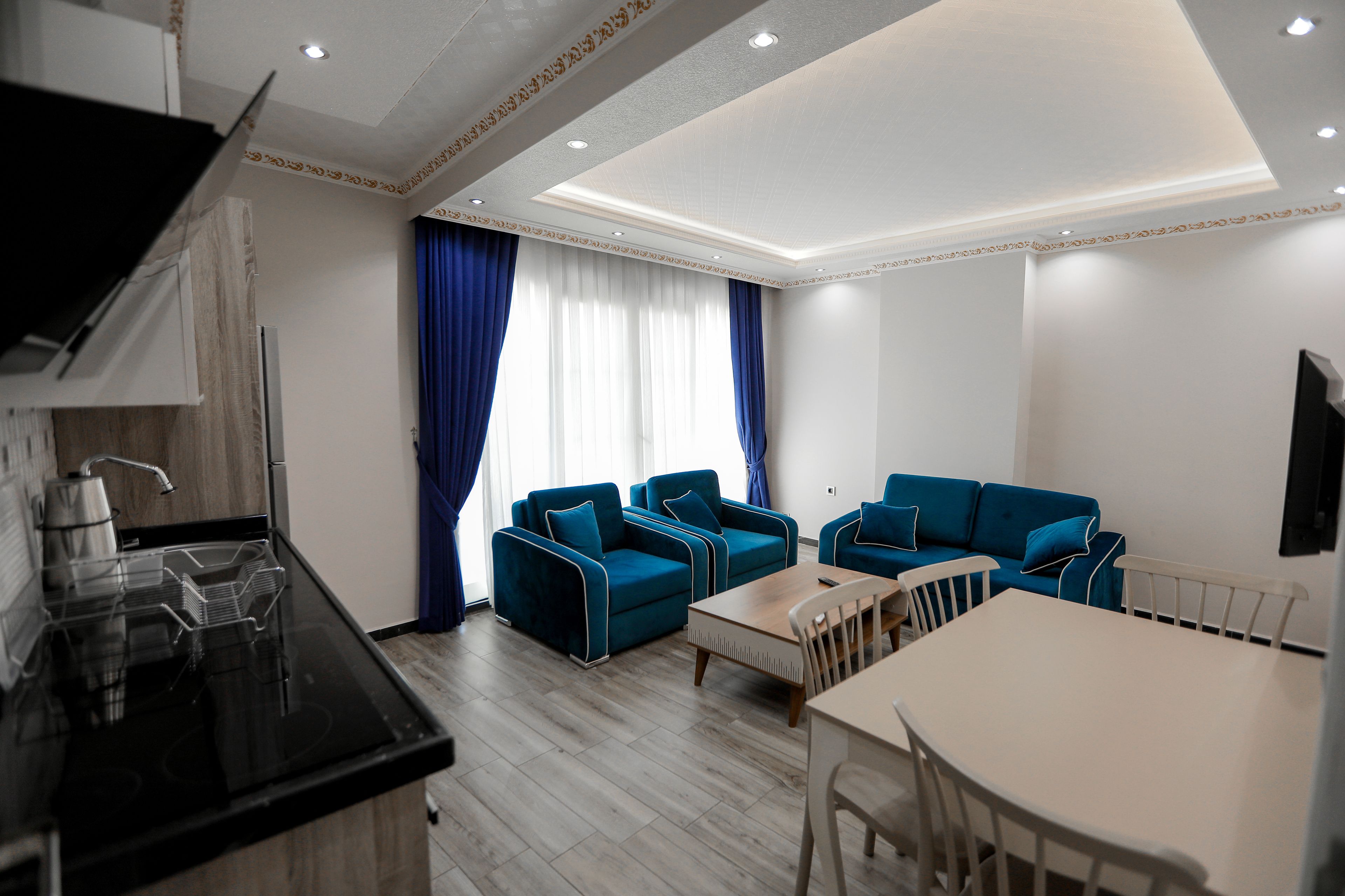A modern living room with a sofa set, a dining table, and a kitchen area with a stove.