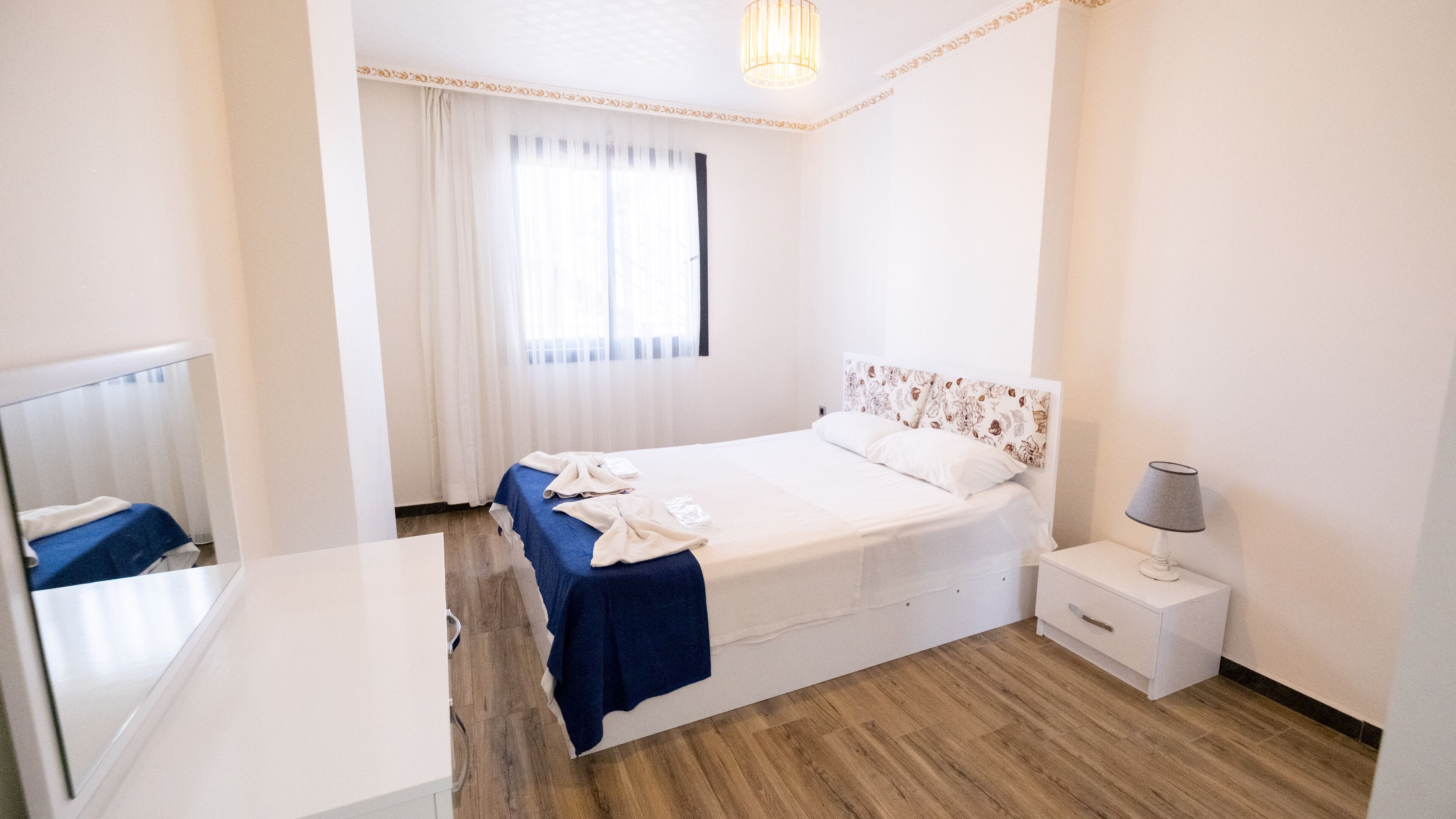 Habitación de hotel con cama, mesita de noche con lámpara, espejo y ventana con cortinas.