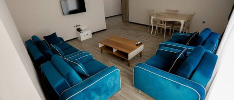 Una sala de estar moderna con un sofá, una mesa de centro de madera, un televisor montado en la pared y una zona de comedor con sillas.