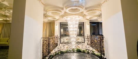 Una imponente escalera con suelo de mármol, barandilla de metal ornamentada y un candelabro.