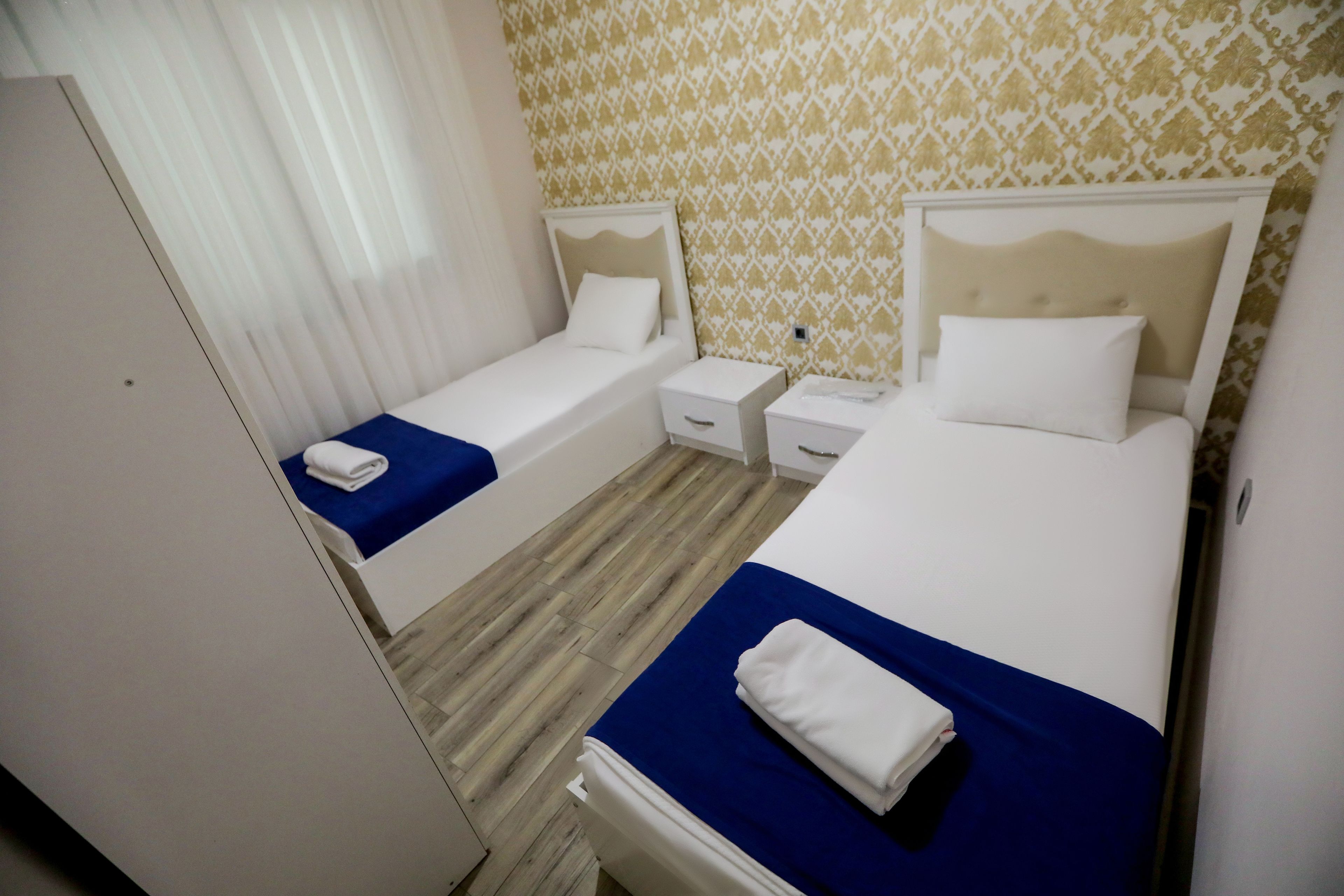 A hotel room with two single beds, a small bedside table with a lamp, and a wardrobe.