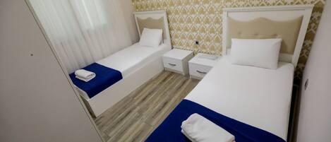 Una habitación de hotel con dos camas individuales, una mesita de noche pequeña con lámpara y un armario.