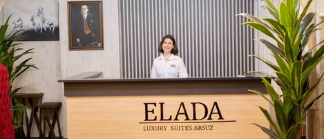 Una recepción con el nombre "ELADA LUXURY SUITES/ARSUZ" y un retrato enmarcado en la pared.