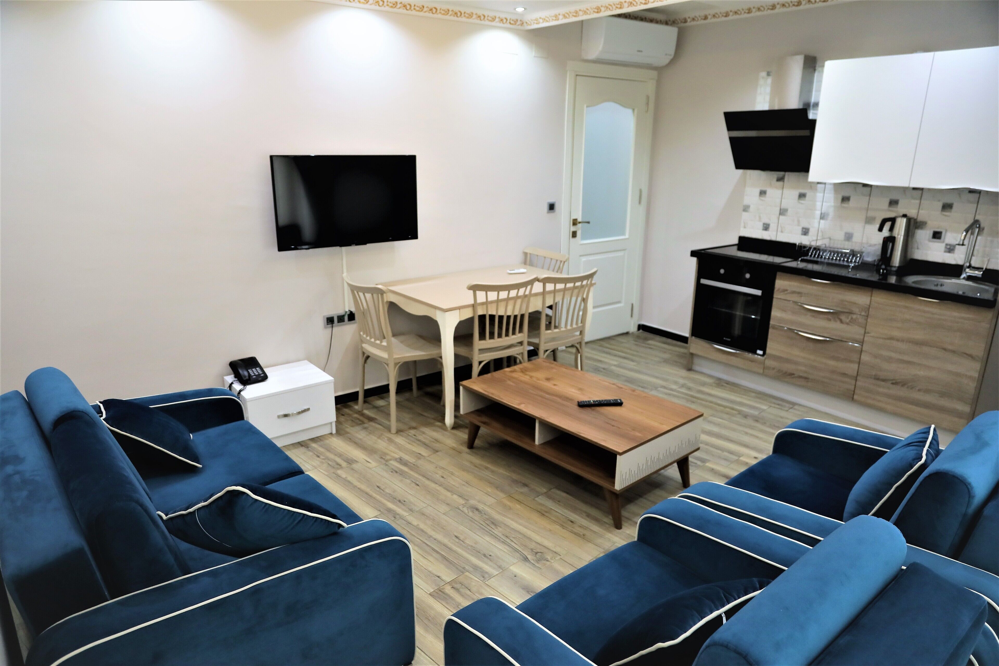 A modern living room with blue sofas, a wooden coffee table, and a TV mounted on the wall.