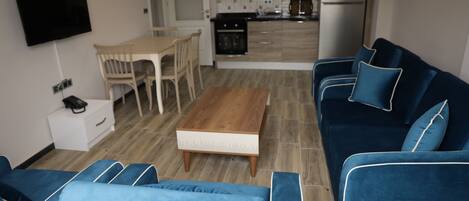 Una sala de estar moderna con un sofá azul, una mesa de centro de madera y un televisor montado en la pared.