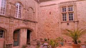 A courtyard with stone buildings, arched doorways, and potted plants. - Château de Puichéric (Puicheric)