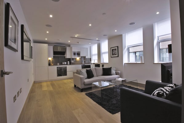 A modern living room with a sofa, coffee table, and a kitchen in the background.