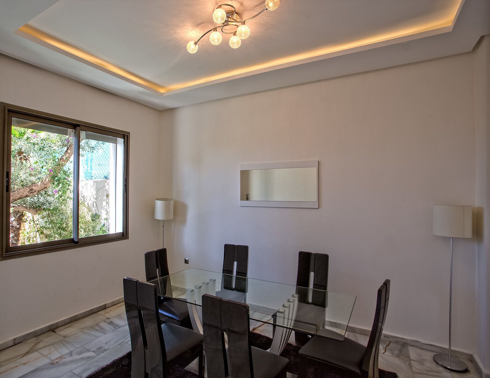 A modern meeting room with a glass table, six chairs, two floor lamps, and a ceiling light fixture.