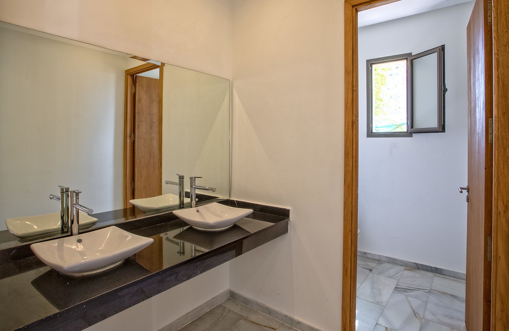 Une salle de bain avec deux lavabos, un grand miroir et une porte donnant sur une autre pièce.