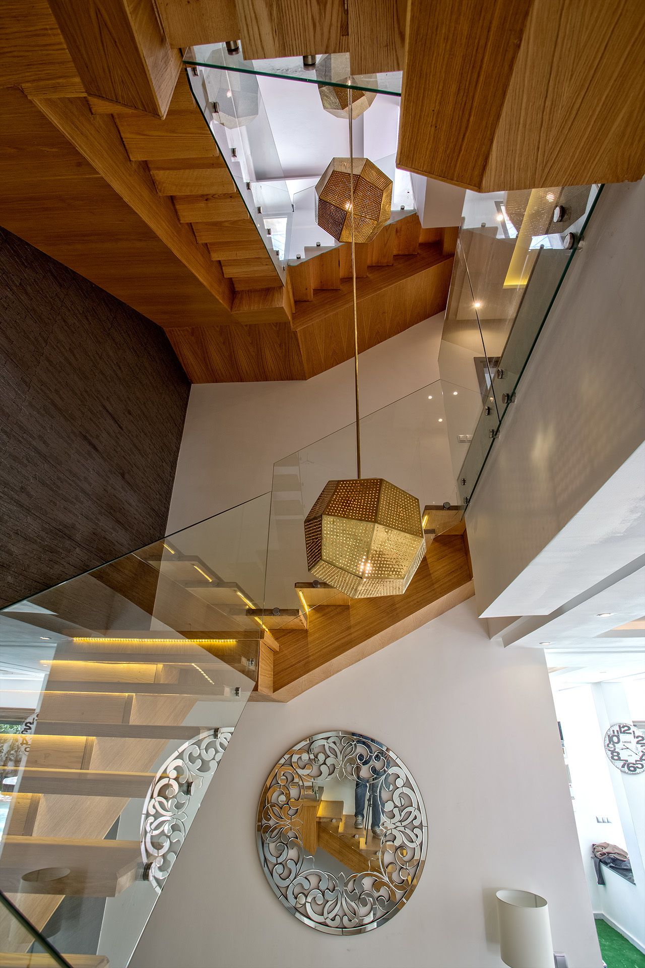 A modern interior with a glass staircase, wooden beams, and decorative lighting fixtures.