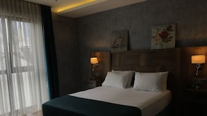 A modern hotel room with a large bed, two bedside lamps, a nightstand, and a window with sheer curtains. - Dedehan Otel (Arsin)