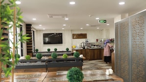 A hotel lobby with a reception area, a TV mounted on the wall, and a sign indicating the exit. - Dedehan Otel (Arsin)