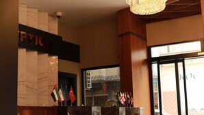 A hotel reception area with a marble counter, flags, and a chandelier. - Dedehan Otel (Arsin)