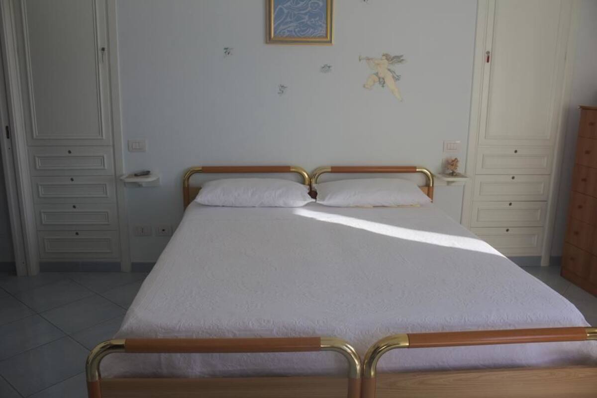 Um quarto com uma cama de solteiro, mesa de cabeceira, cômoda e guarda-roupa.