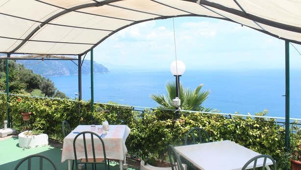 Un patio al aire libre con mesas y sillas, una marquesina y vistas al mar y las montañas.