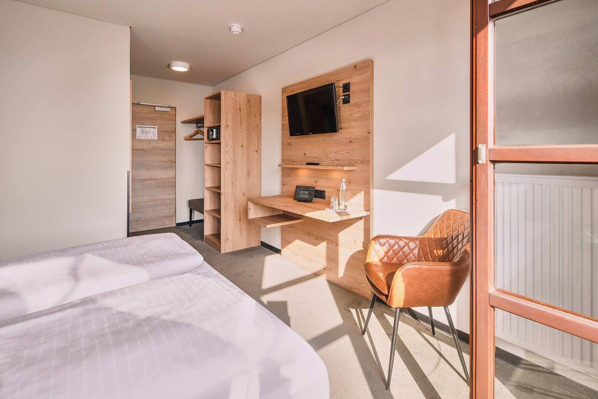 A hotel room with a bed, a desk with a chair, a television, and a radiator.