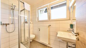 Un bagno con cabina doccia in vetro, un water, un lavandino e una finestra sopra lo specchio.