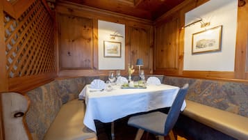 Un comedor con detalles de madera, una mesa blanca dispuesta con copas de vino, una lámpara y un cuadro en la pared.
