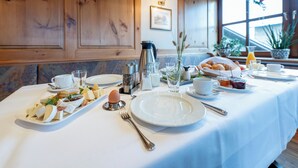 A breakfast table set with plates, bowls, and utensils, a coffee pot, and a window with plants. - Hotel-Restaurant Berghof (Petersberg)