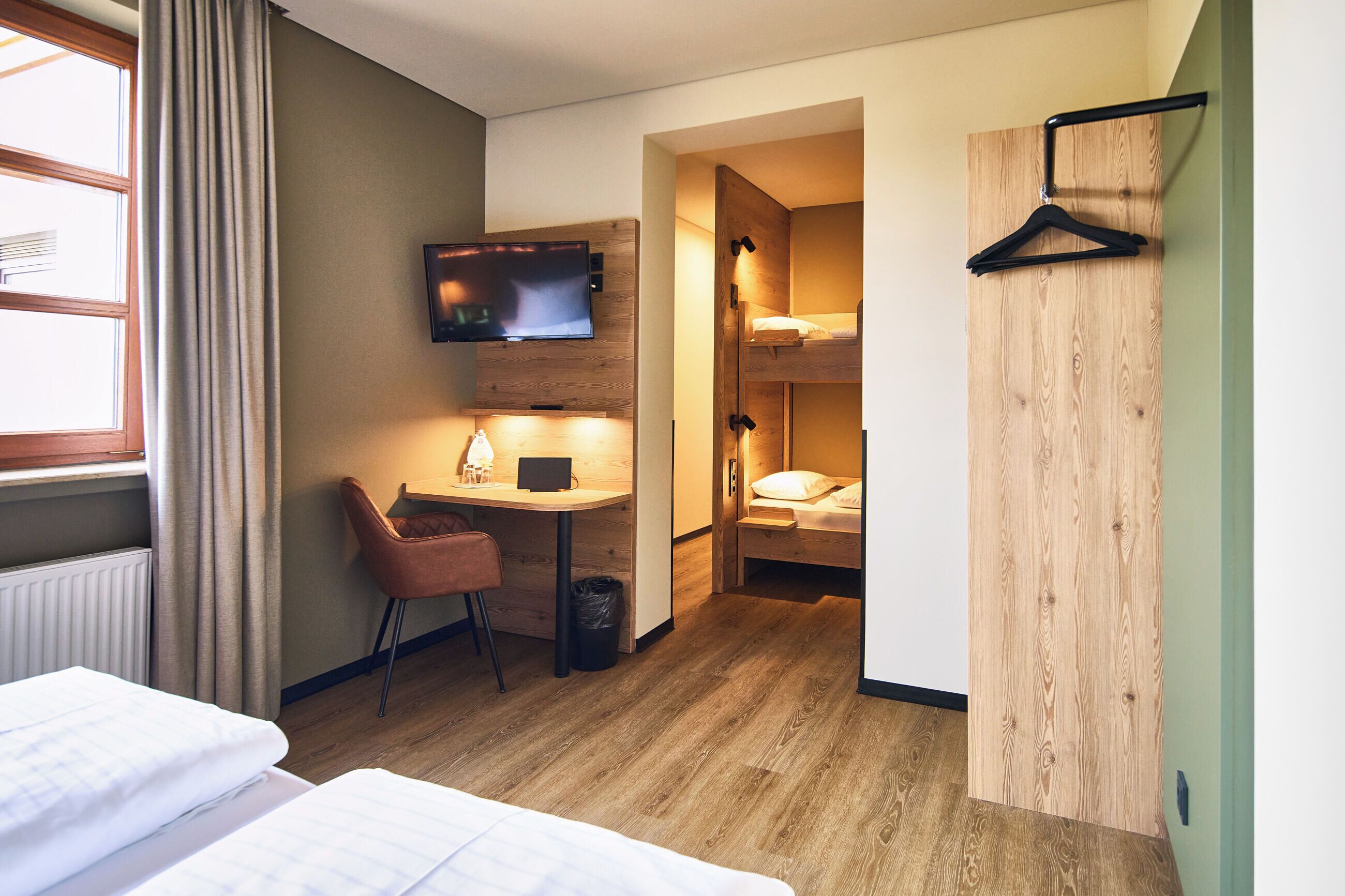 A hotel room with a bed, a desk with a chair, a television, and a wooden wardrobe.