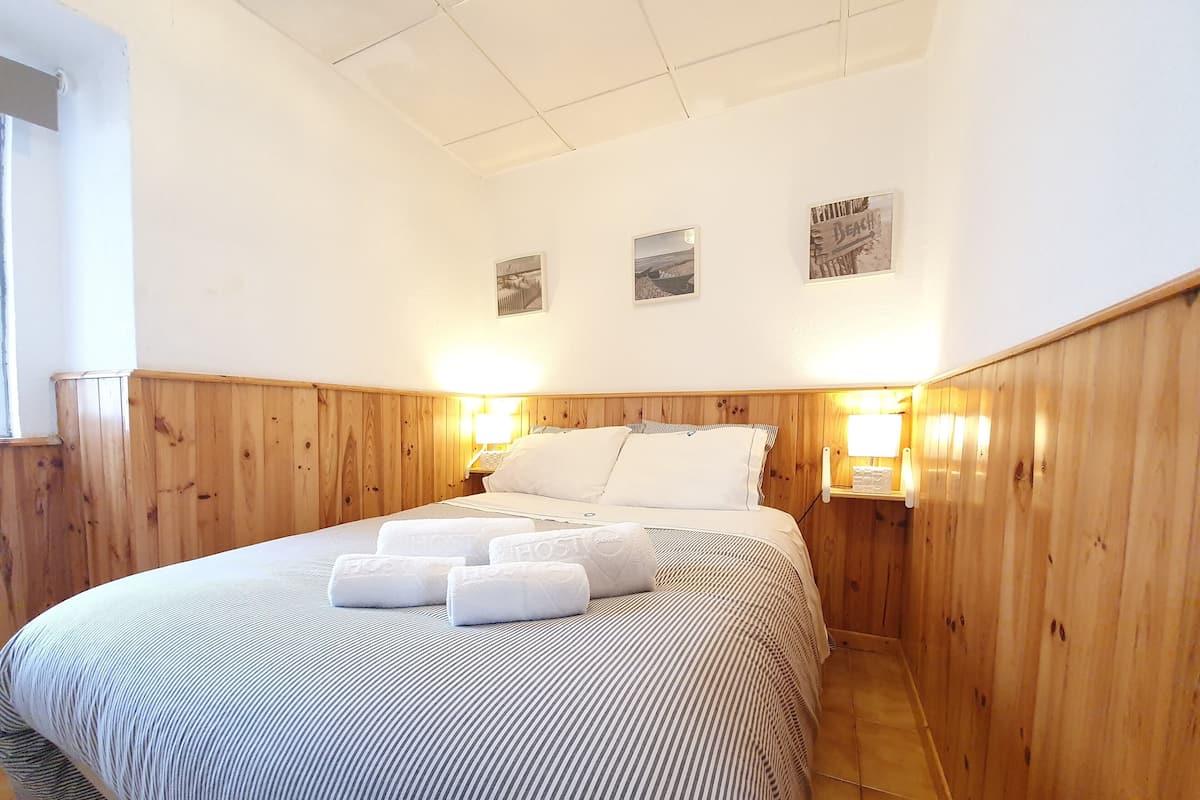 Une chambre d’hôtel avec une tête de lit en bois à panneaux, un lit avec une literie à rayures, deux lampes de chevet et un tableau accroché au mur.