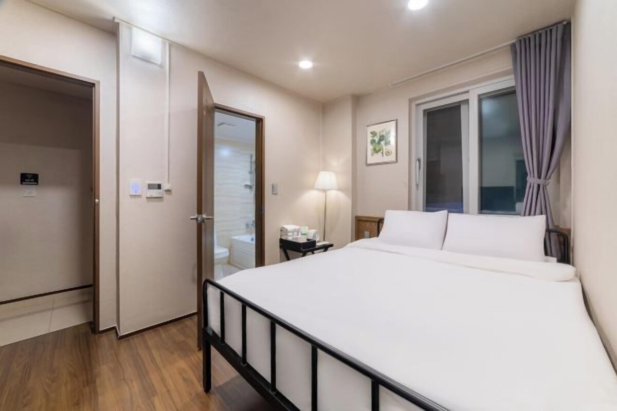 Une chambre d’hôtel avec un lit, une table de chevet, une lampe, une fenêtre avec des rideaux et une porte.